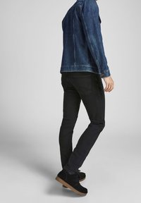 Chaqueta vaquera de color azul oscuro, con mangas largas y bolsillos delanteros, combinada con unos vaqueros negros de corte ajustado. El modelo lleva zapatos de ante negros.