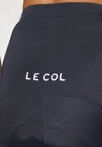 Črne kolesarske kratke hlače iz elastične tkanine, ki na hrbtni strani vsebujejo belo vezeno logo "LE COL" in brezšivno šivanje.