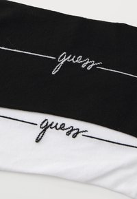 Sorte og hvide bomuldsstrømper med broderet "guess" tekst med understregning, glat tekstur og kontrastfarver på hver strømpe.