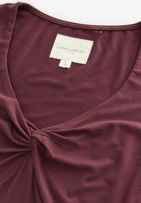 Top burdeos hecho de tela suave con un diseño de escote en V y un detalle anudado en la cintura. Etiqueta que dice "Laura Ashley", talla S.