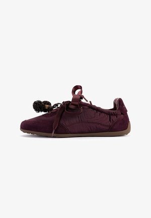 Zapatilla plana burdeos con paneles de ante y tela, borlas decorativas en los cordones y suela de goma marrón.