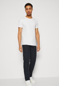 White short-sleeve t-shirt paired with navy pants and white sneakers. The fabric appears smooth with a fitted shape and crew neckline.