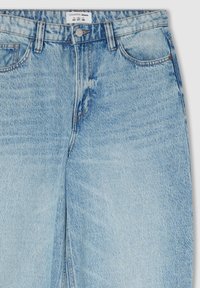 Jasnoniebieskie dżinsy wykonane z denimu o klasycznym pięciokieszeniowym kroju, z subtelnym efektem przetarcia, przeszyciami i pojedynczym zapięciem na guzik.