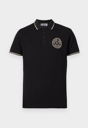 Polo noir avec bordure beige sur le col et les manches, patte de boutonnage, et logo rond Versace Jeans Couture sur la poitrine gauche.