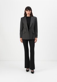 Šedý pruhovaný dvouřadový blazer s velkými klopami, spárovaný s černým topem a rozšířenými černými kalhotami. Černé lodičky dokončují vzhled.