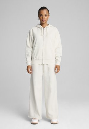 Felpa bianca con zip, cappuccio e cordini, abbinata a pantaloni larghi coordinati. Tessuto borgogna su tutta la superficie.