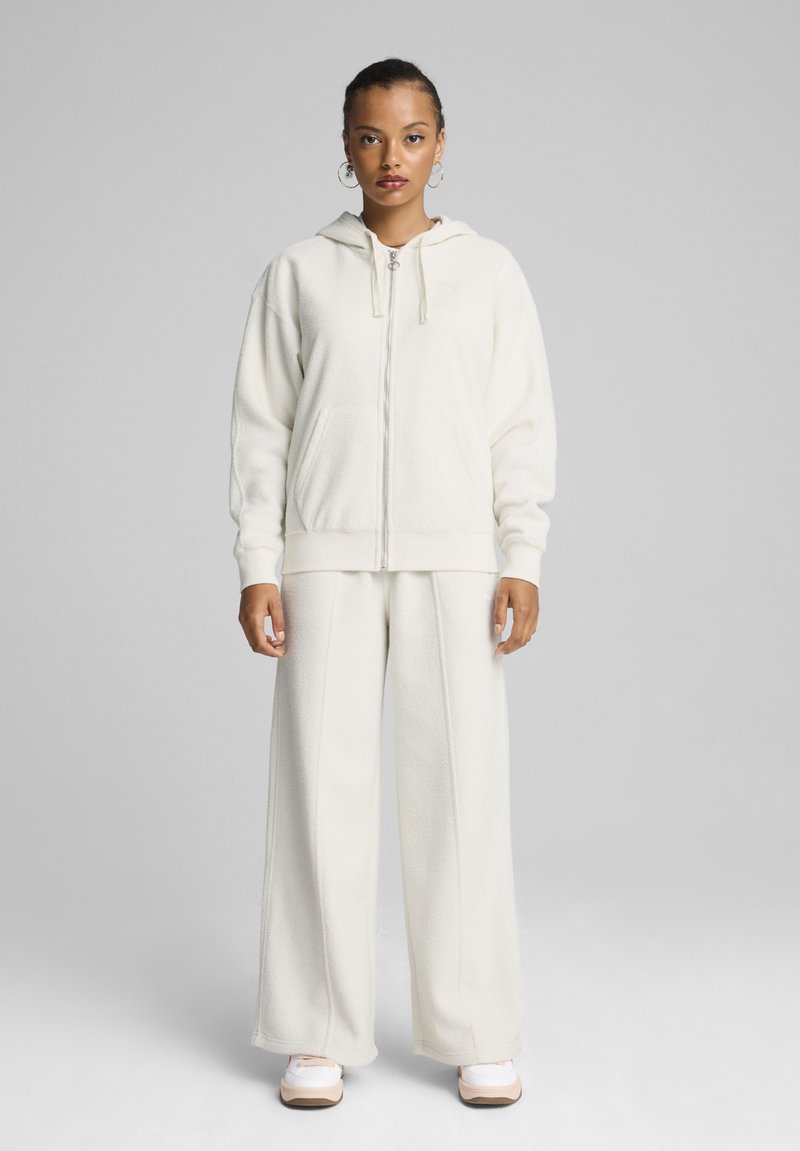 Felpa bianca con zip, cappuccio e cordini, abbinata a pantaloni larghi coordinati. Tessuto borgogna su tutta la superficie.