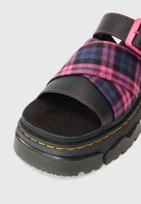 Sandal in pelle nera e tessuto a quadri viola con design a punta aperta, dotato di una fibbia rosa e suola chunky nera con cuciture gialle.