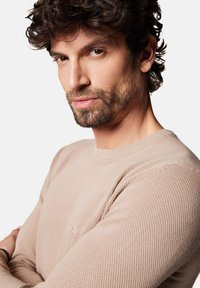 Jasno beżowy sweter z dzianiny z okrągłym dekoltem, teksturowanym materiałem i szczegółowym haftem na ramionach. Dyskretne logo na piersi.