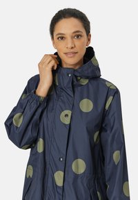 Marine vandtæt jakke med store olivengrønne prikker, elastiske manchetter, trykknapper og hætte. Glat, let materiale.