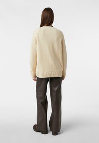 Kremowy sweter dziergany o fakturowanym wykończeniu, zestawiony z wysokim stanem brązowych skórzanych spodni i platformowymi botkami.