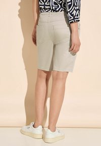 Beige shorts with a mid-rise waist and back pockets. Worn with white sneakers. Smooth texture, casual design, and knee-length cut.