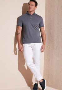 Heathergrå polo med spetsig krage, parat med vita byxor. Outfiten fulländas med marinblå sneakers.