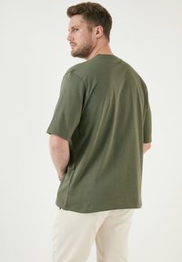 Zelené tričko s krátkým rukávem vyrobené z bavlny, s volným střihem a kulatým výstřihem. Jednoduchý design bez viditelných vzorů nebo akcentů.