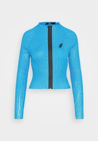 Blå ribbad jacka med hög krage, full dragkedja fram och långa ärmar. Har en svart logotyp på vänster bröstområde.