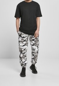 Schwarzes Baumwoll-T-Shirt kombiniert mit weißen und grauen Camo-Sweatpants. Die Hose hat elastische Bündchen und einen lässigen Schnitt. Schwarze Sneakers als Fußbekleidung.