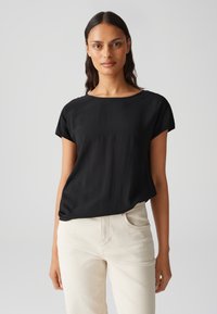 Top nero a maniche corte con scollatura rotonda, realizzato in un tessuto morbido, abbinato a pantaloni chiari per un contrasto. Design semplice ed elegante.