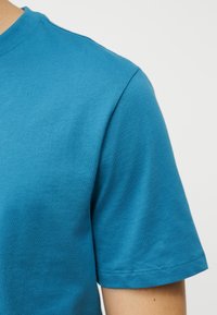 Κοντινό πλάνο ενός ατόμου που φοράει απλό μπλε βαμβακερό κοντομάνικο μπλουζάκι σε απλό ανοιχτό φόντο.