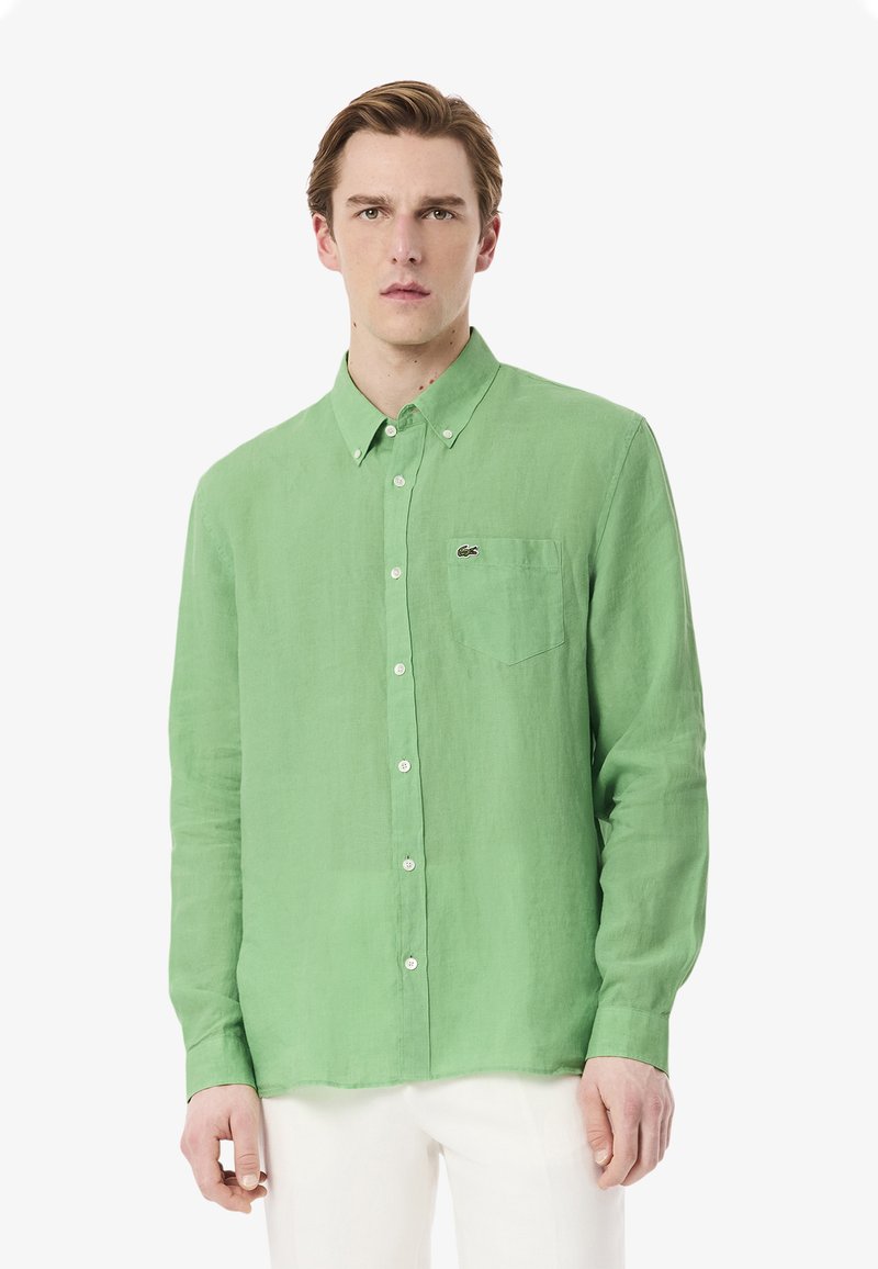 Camicia di lino verde con colletto button-down, maniche lunghe e taschino sul lato sinistro con logo. Texture liscia, vestibilità sartoriale.