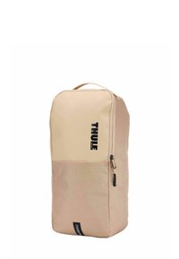 Sac à dos Thule en beige avec un panneau supérieur lisse et une section inférieure texturée. Il présente un logo, un tirette de fermeture éclair, une forme rectangulaire et une poignée de transport.