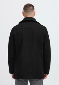 Schwarzer Wollmischmantel mit Kragen, gerade geschnitten, sichtbaren Nähten und langen Ärmeln. Die Rückansicht zeigt ein einfaches, sauberes Design.