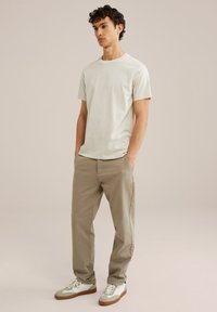 Tricou cu gât rotund, bej deschis, asortat cu pantaloni bej deschis, și adidași albi cu accente gri. Croi lejer, textură netedă, design minimalist.