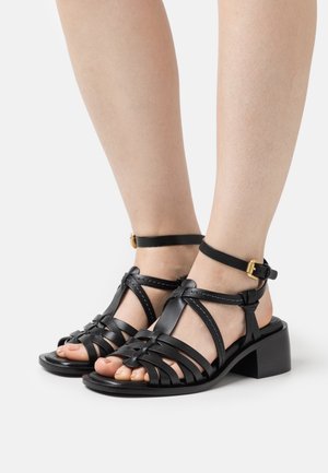 Zwarte leren sandalen met hak, voorzien van een geweven design, enkelbandje en rechthoekige blokhak. Gladde textuur en minimale stikseldetails.