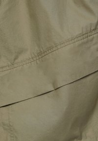 Tissu kaki, texture lisse, détails de couture visibles, design en couches avec un léger éclat, mettant en valeur des tons de couleur neutres.