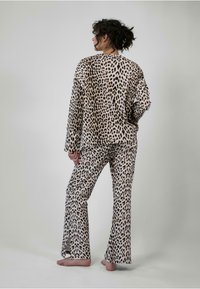 Pyžamový set s leopardím vzorom, ktorý obsahuje dlhý rukáv a rozšírené nohavice v béžovej a hnedej farbe, vyrobený z jemnej a hladkej tkaniny.