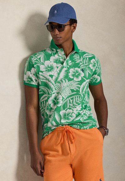 Πράσινο πόλο πουκάμισο με λευκό ανθικό μοτίβο, κοντά μανίκια και γιακά; σετ με πορτοκαλί σορτς. Διαθέτει επίσης μπλε καπέλο και γυαλιά ηλίου.