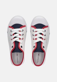 Zapatillas de lona blancas con detalles en azul marino y ribete rojo, que cuentan con una puntera redonda, diseño con cordones y logo en la plantilla.
