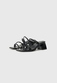Black heeled sandals feature a square toe and curved straps. The textured heel is block-shaped, providing stability and a modern design.