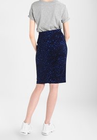 Mörkblå kjol med strukturerad, mönstrad tyg, figurnära design och medellång längd, kombinerad med en kortärmad grå topp och vita sneakers.