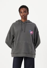Hoodie surdimensionné gris en tissu doux, avec un graphique en forme de cœur portant "TOMMY JEANS". Équipé d'une poche avant et d'une capuche à cordon.