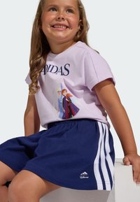 Fialové tričko s grafikou s nápisom "Adidas" a postavičkami z Disneyho, v kombinácii s námorníckymi modrými šortkami s bielymi bočnými pruhmi a elastickým pásom.