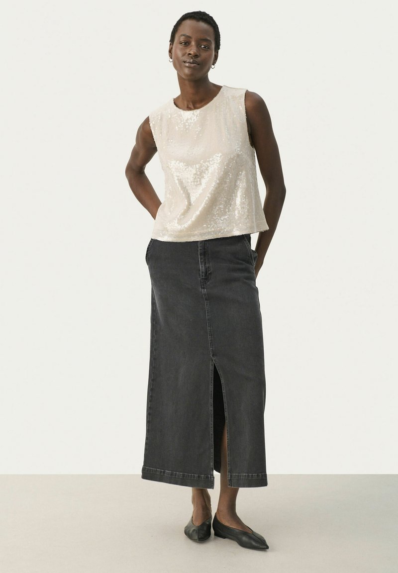 Kremowa bluzka z cekinami i okrągłym dekoltem, połączona z długą czarną spódnicą dżinsową z rozporkiem z przodu i casualowym krojem. Całość dopełniają czarne baleriny.