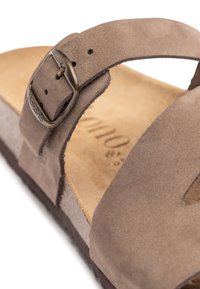 Bruine suède sandaal met een brede band, verstelbare metalen gesp en een gestructureerde kurken zool. Het interieur heeft een gladde, beige voetbed.