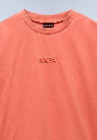Koralli puuvillapaita, jossa on pyöreä kaulus ja teksturoidulla "NAPA"-logolla brodeerattu rinta. Silkkinen kangas ja rento malli.