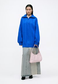 Suéter azul de punto trenzado con cuello de cremallera, combinado con un bolso de mano rosa claro y una falda larga de mezclilla gris con un detalle de costura.