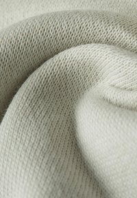Tessuto beige chiaro e morbido con una fine trama a maglia, caratterizzato da una forma liscia e arrotondata e dettagli sottili nel filo.