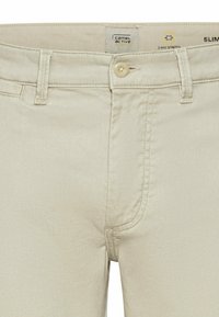 Pantaloni beige slim-fit con chiusura a bottone e quattro tasche. Realizzati in tessuto stretch a due vie, presentano una superficie liscia e testurizzata.