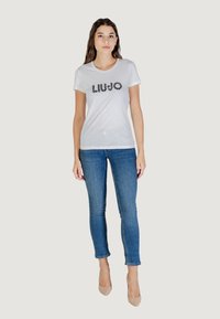 T-shirt bianca in cotone a maniche corte, con il nome del marchio "LIU JO" stampato in nero. Abbinata a jeans skinny in denim blu.