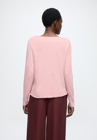 Hosszú ujjú, világos rózsaszín felső kerek nyakkivágással és enyhén ívelt szegéllyel, sötét bordó széles szárú nadrággal párosítva. Puha tapintású anyag.