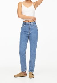 Jeans de tiro alto en azul claro, fabricados en denim, con un diseño clásico de cinco bolsillos y un ligero desgastado. Combinados con una blusa blanca con borde de encaje.