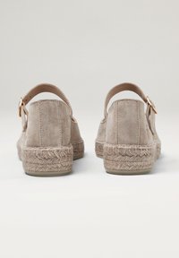Zapatos de esparto de ante beige con tira trasera, que cuentan con suelas de yute trenzado y un acento de hebilla en tono dorado. Suela plana de goma.