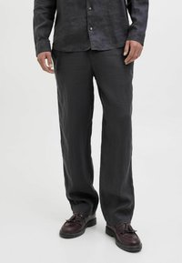 Chemise et pantalon en lin noir, coupe ample, texture subtile, assortis à des chaussures à lacets marron foncé avec un détail pompon.