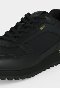 Μαύρο δερμάτινο και υφασμάτινο sneaker με υφασμένη σόλα, μαύρα κορδόνια και χρυσό λογότυπο "BOSS" στο πλάι κοντά στη φτέρνα.
