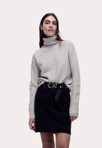 Maglione a collo alto grigio chiaro in maglia abbinato a una mini gonna in velluto nero, con una cintura nera con fibbia metallica e dettagli.