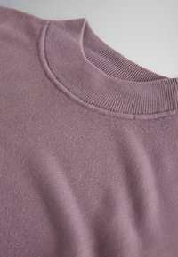 Primer plano de un jersey de punto morado polvoriento que muestra cuello redondo acanalado y tejido de textura suave.