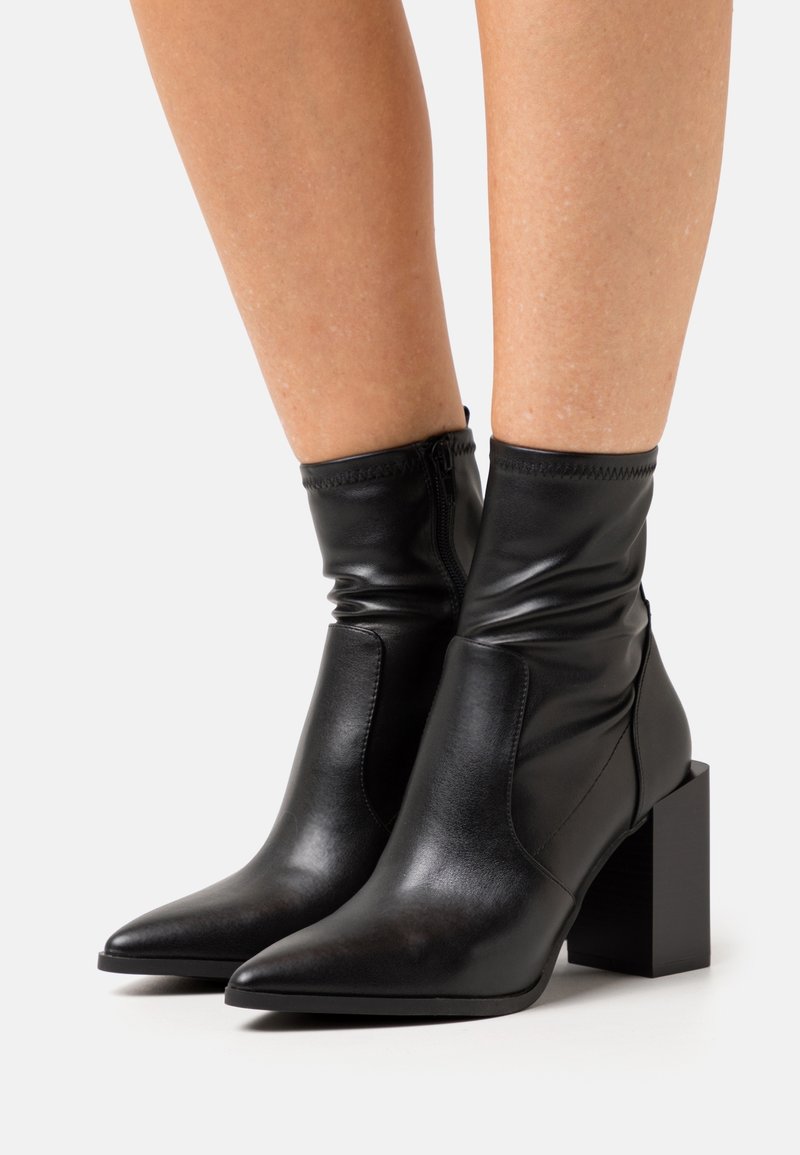 Stivali ankle in pelle nera con punta a punta e tacco a blocco. Presentano una texture arricciata attorno alla caviglia e una chiusura con zip sul retro.